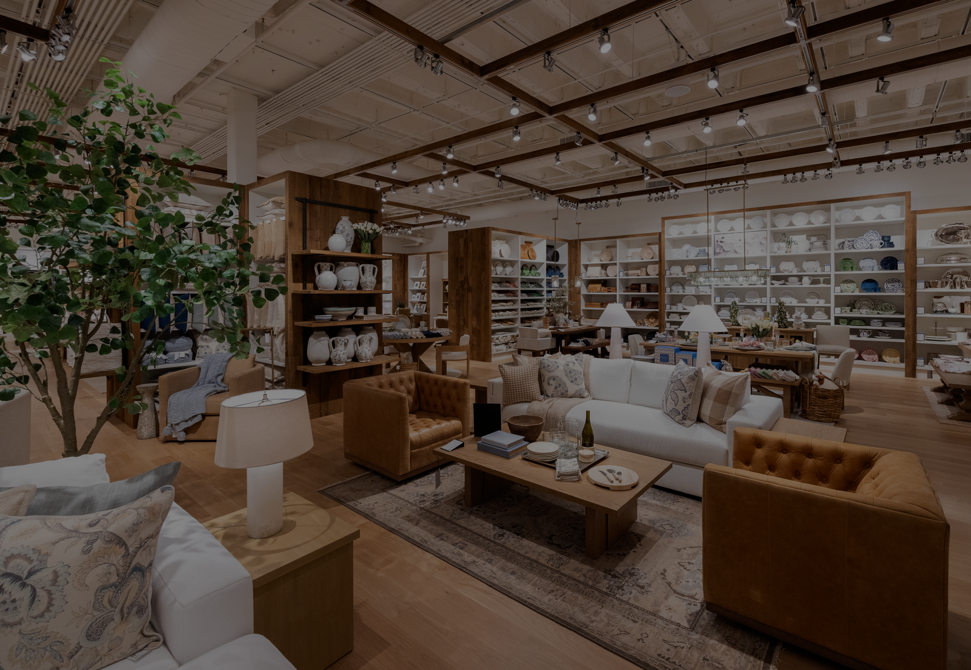 An interior shot of a Pottery Barn store, featuring chairs and sofa sets in the foreground, and shelves of various dishes and pottery in the background.