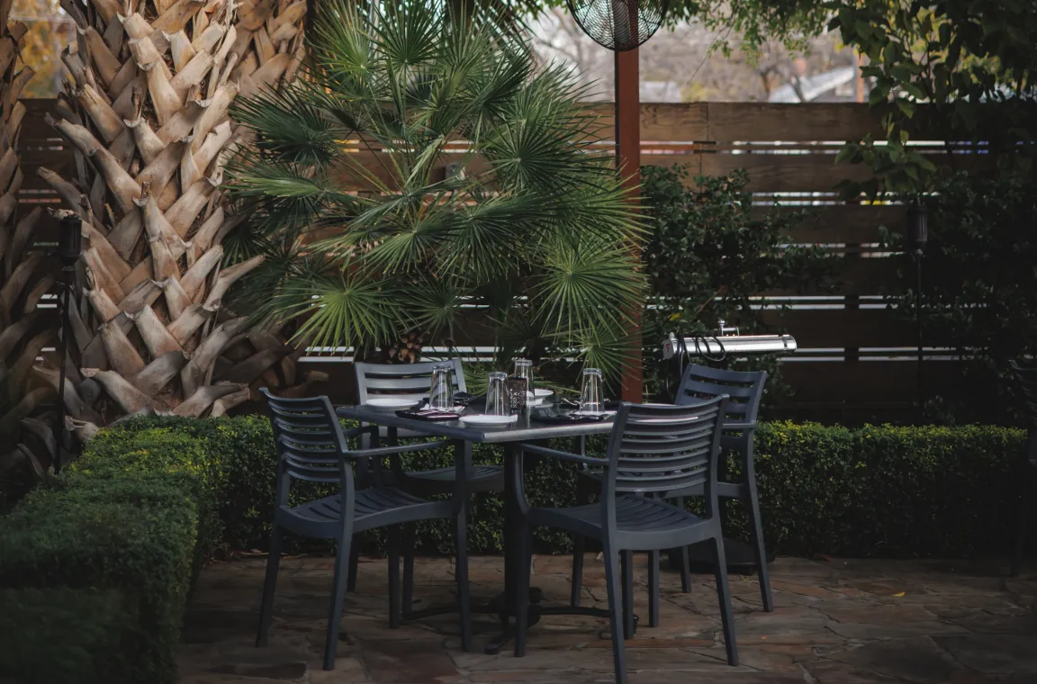 Intimate outdoor patio dining area at Bliss restaurant with a table set for four, surrounded by lush landscaping and palm trees.
