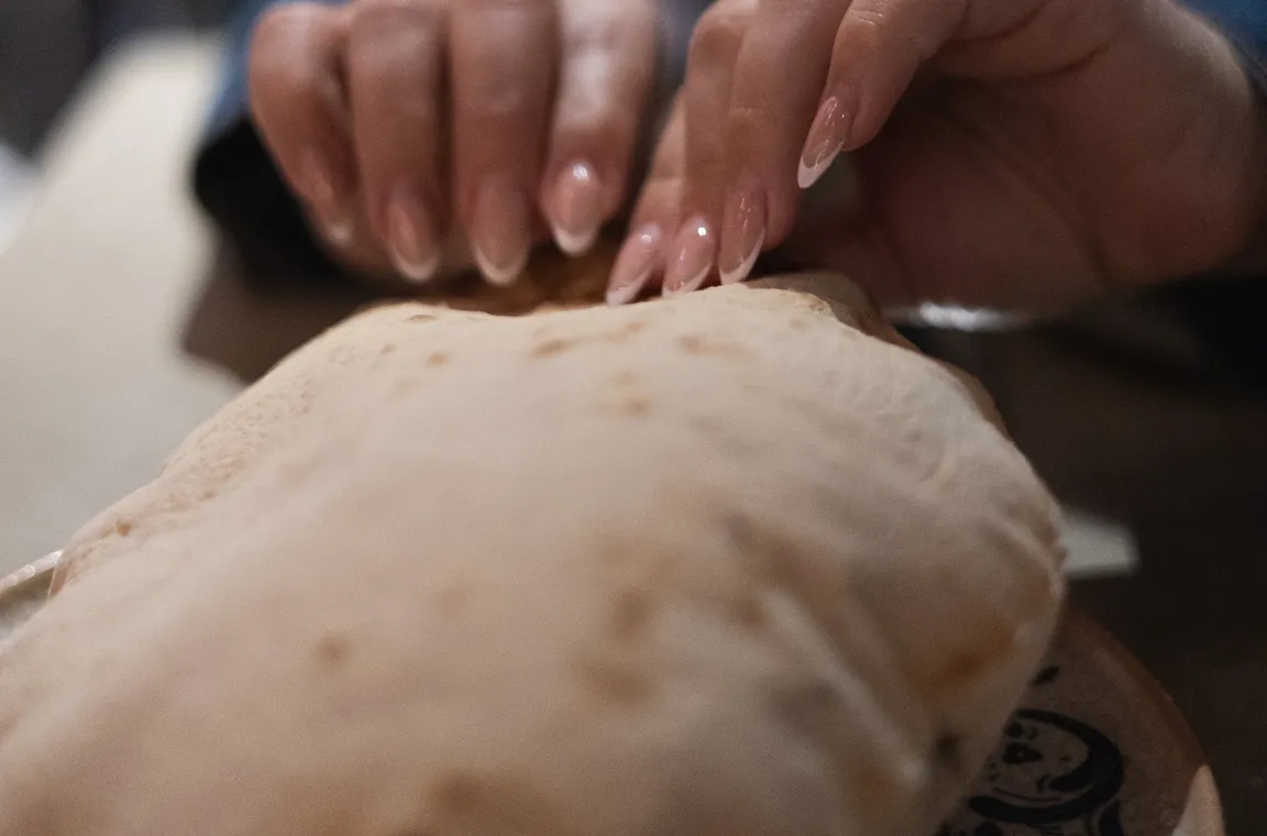 Hands tearing into a warm, freshly baked pita bread served at the table in Ladino restaurant.