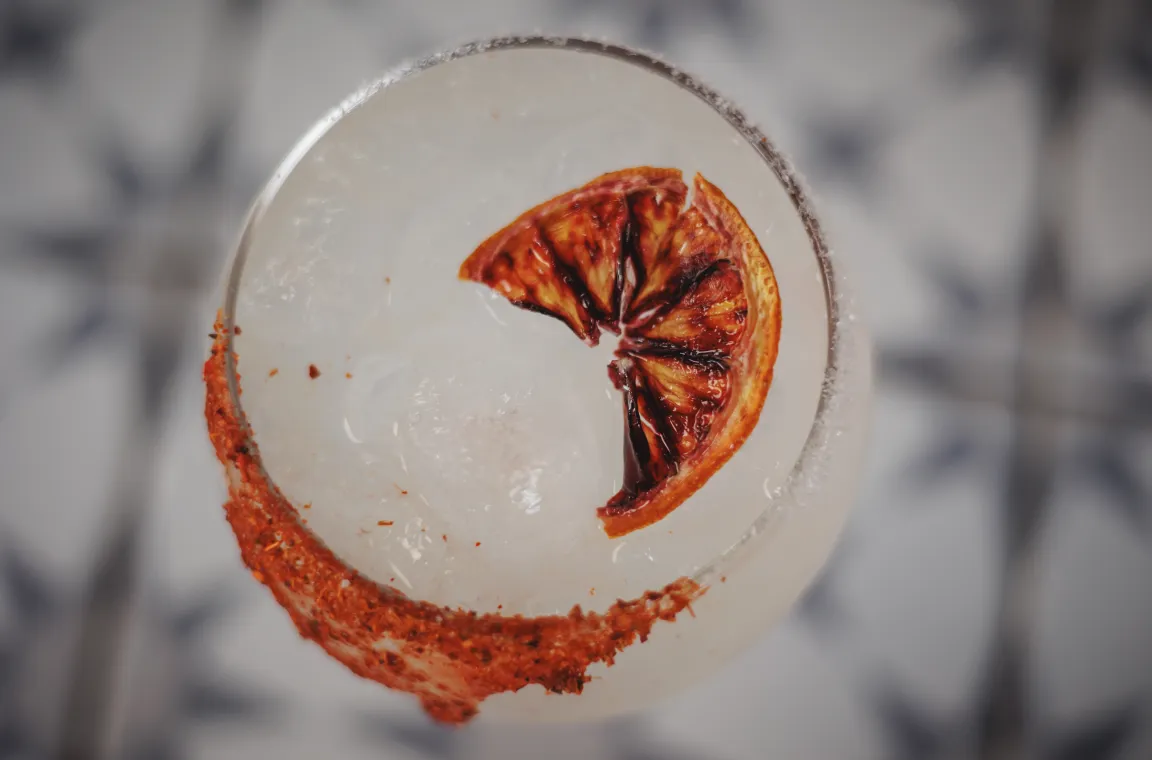 Overhead view of a citrus cocktail at Soluna restaurant, garnished with a charred orange slice and a chili-salt rim.