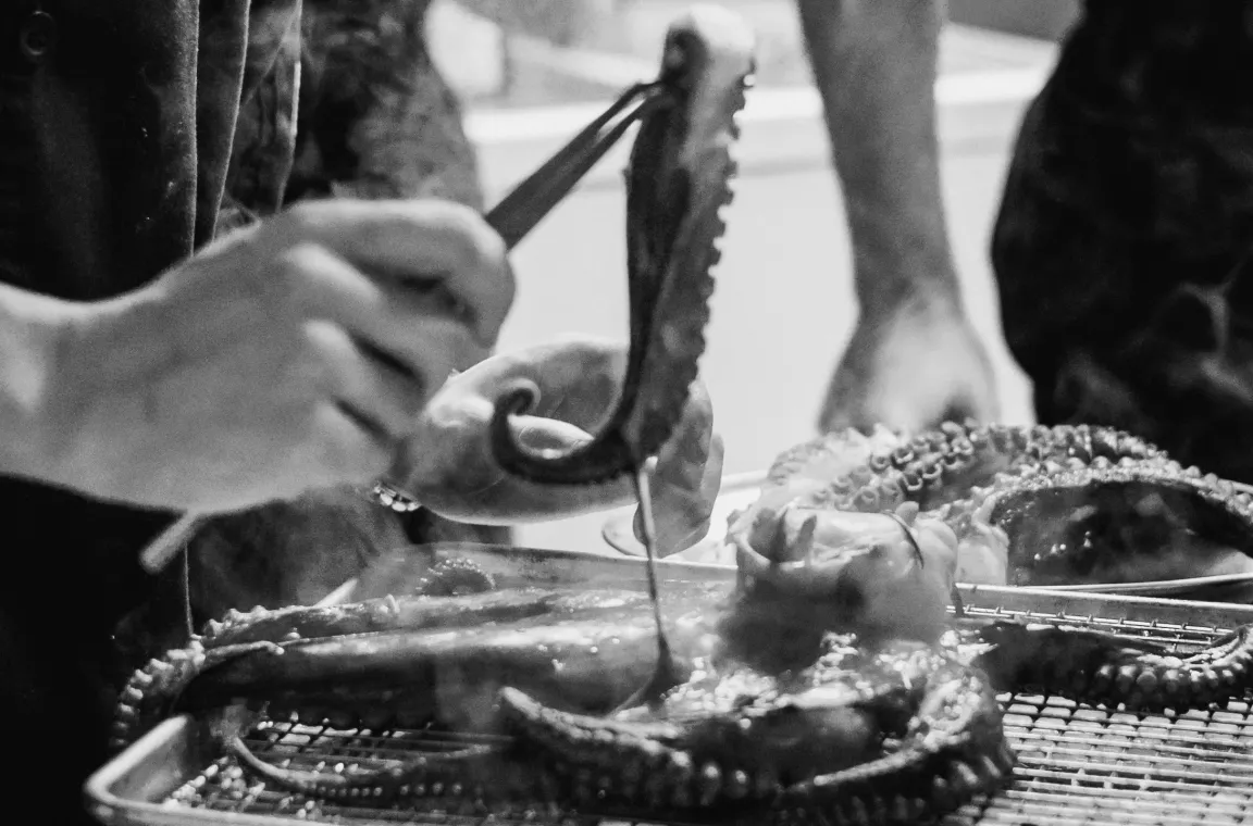 Black-and-white close-up of a chef plating grilled octopus in the kitchen at Bliss restaurant in San Antonio.