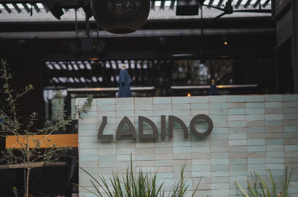Daytime exterior of Ladino restaurant featuring its tiled entrance wall, modern patio seating, and landscaped plants.