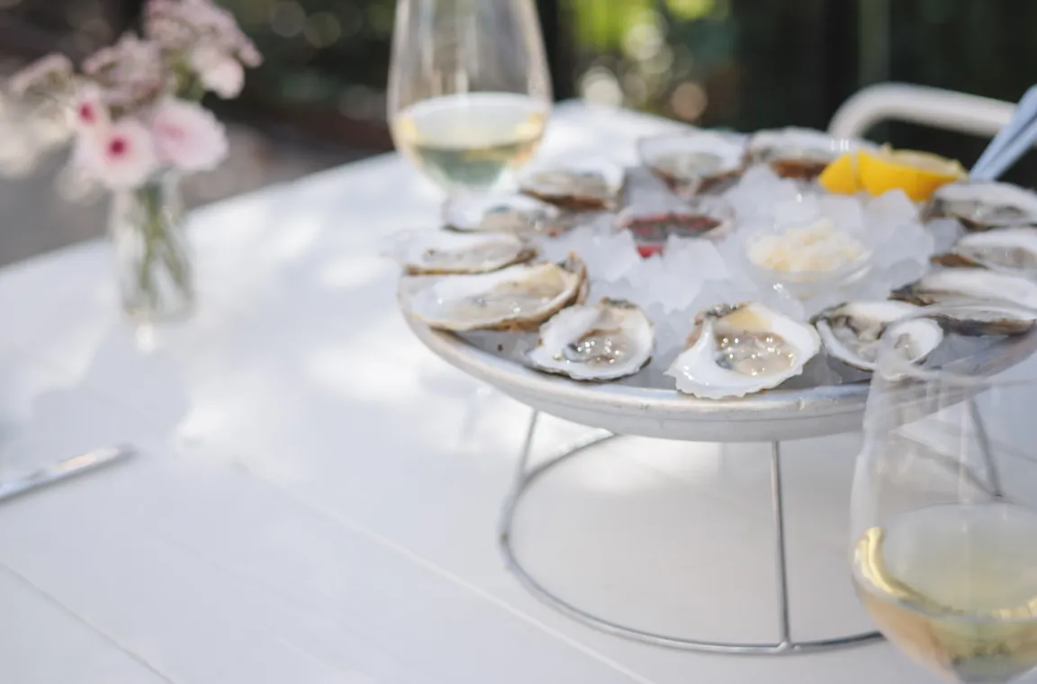 Chilled oyster platter served on ice with lemon, mignonette, and white wine at an outdoor table at Little Em's Oyster Bar.