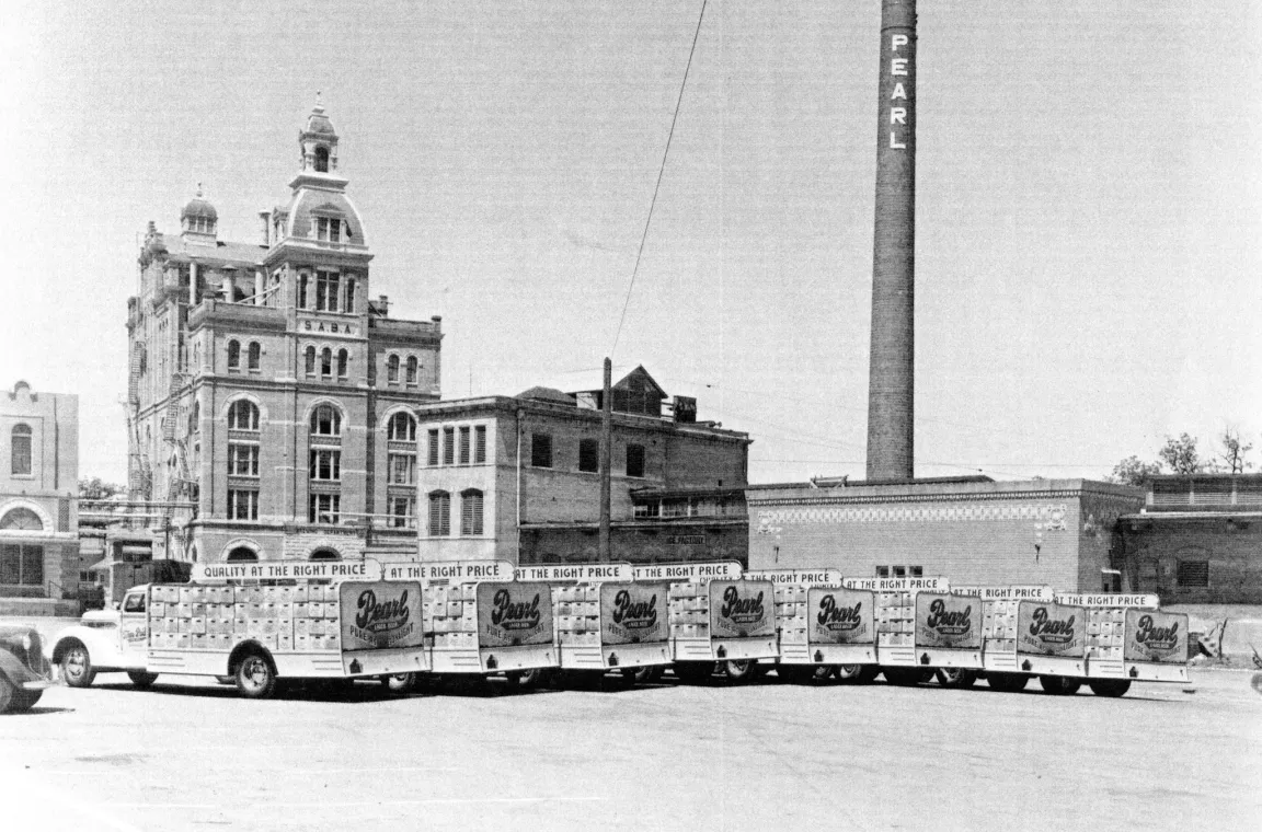 Historic black-and-white photograph of the original Pearl Brewery in San Antonio, featuring delivery trucks lined up outside the brewery with the iconic Pearl smokestack rising above the complex.