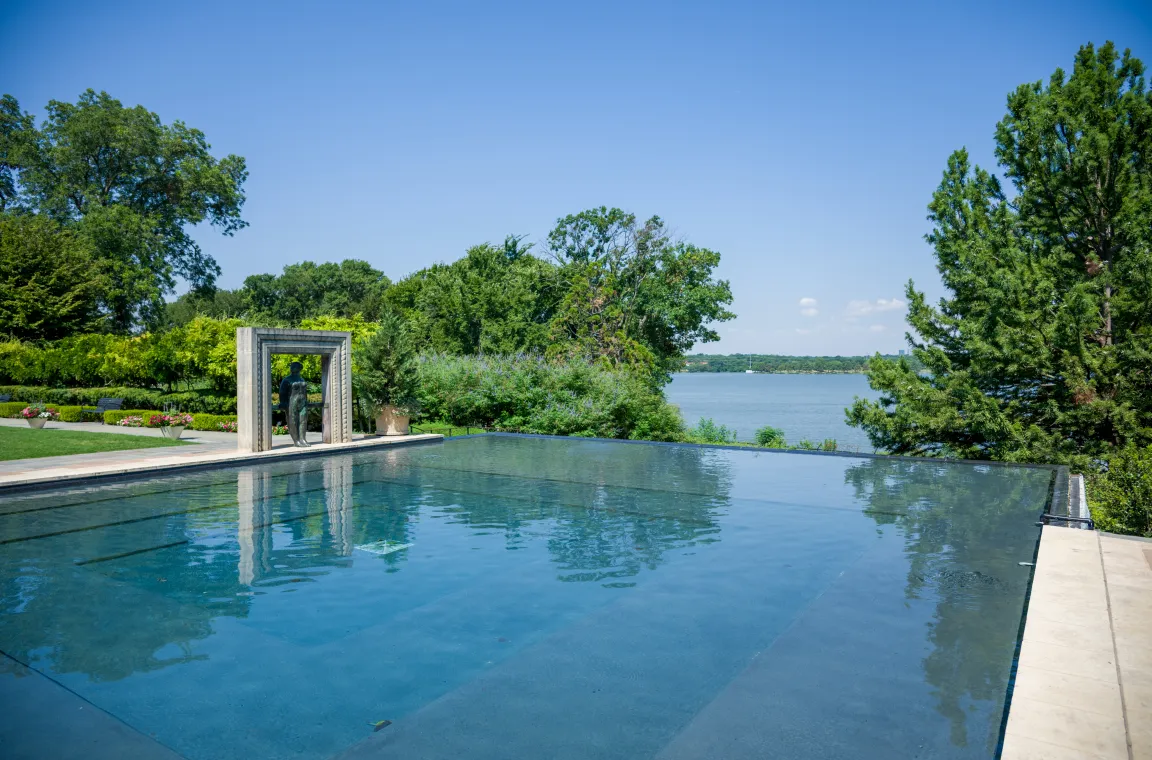 The iconic infinity reflecting pool overlooking White Rock Lake, framed by a sculptural stone arch and meticulously landscaped gardens.