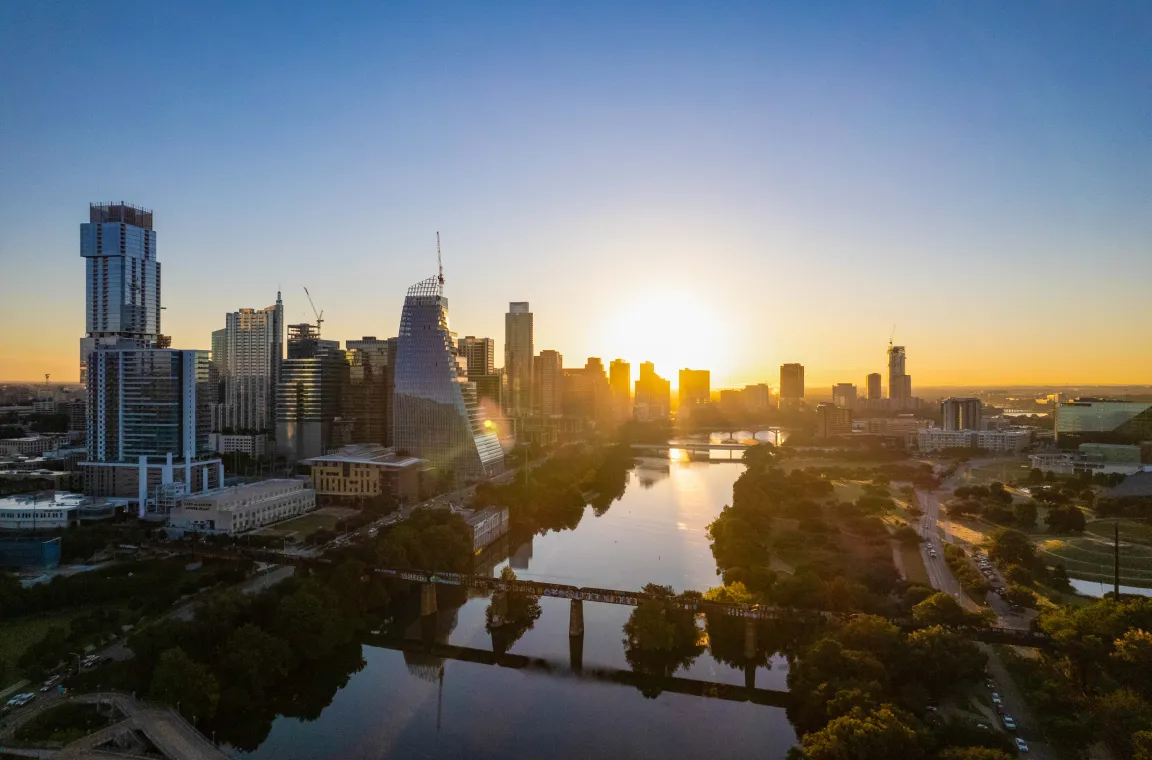 Aerial sunrise view of Lady Bird Lake and the Austin skyline, with golden light reflecting across the river and surrounding parks.