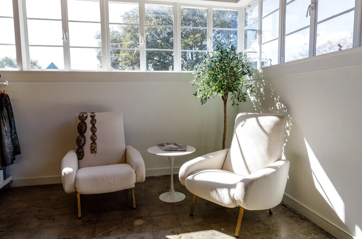 Bright seating area inside Abejas Boutique featuring two modern armchairs, a small side table, and large windows that fill the space with natural light.