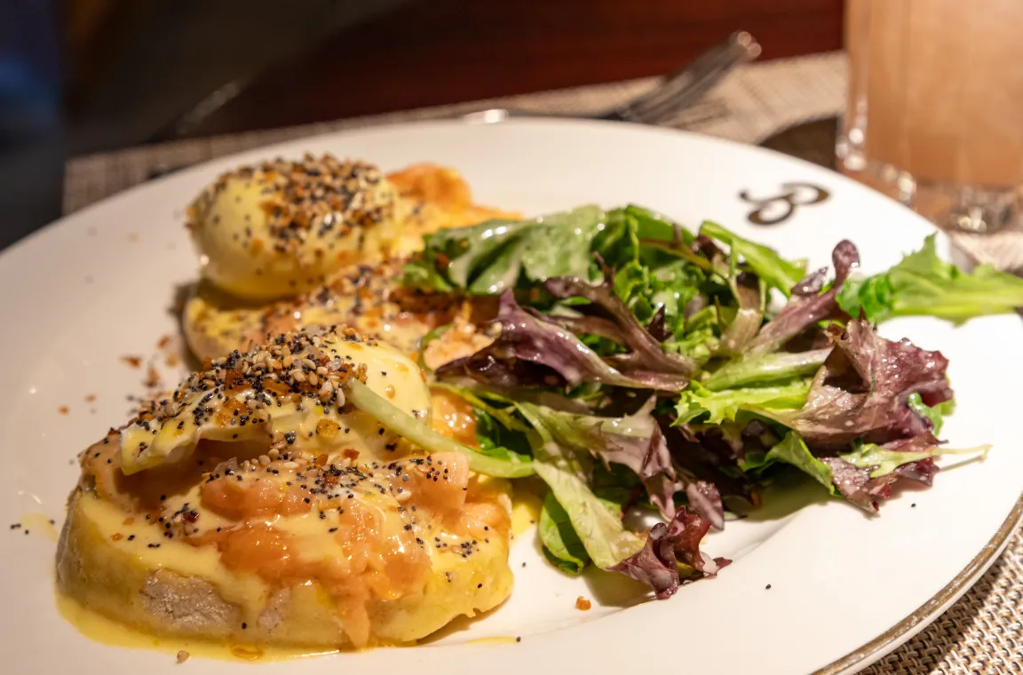 A brunch dish at Bludorn featuring eggs benedict topped with everything bagel seasoning and hollandaise sauce, served alongside a fresh green side salad.