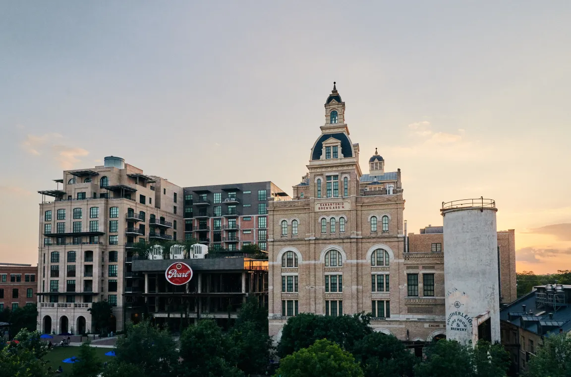 Sunset view of the historic Pearl Brewery building in San Antonio, framed by modern apartments and restored industrial structures.