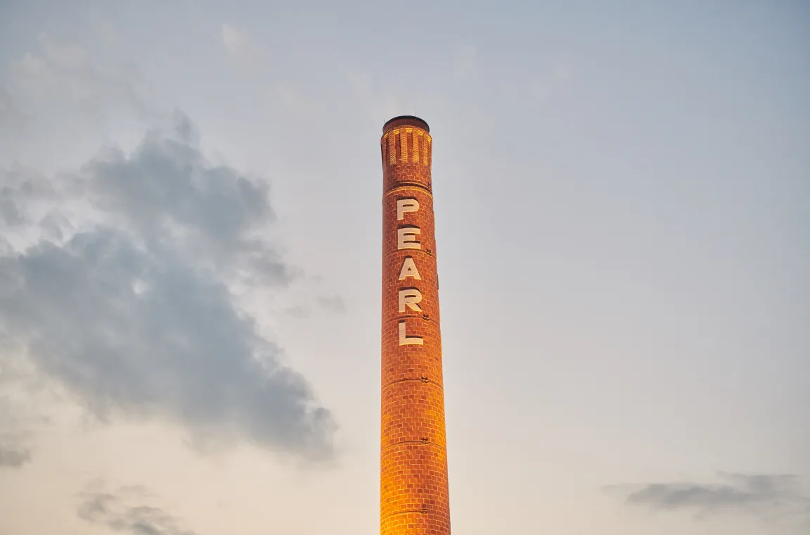 Close-up of the illuminated Pearl smokestack glowing at dusk beneath soft clouds in the San Antonio skyline.