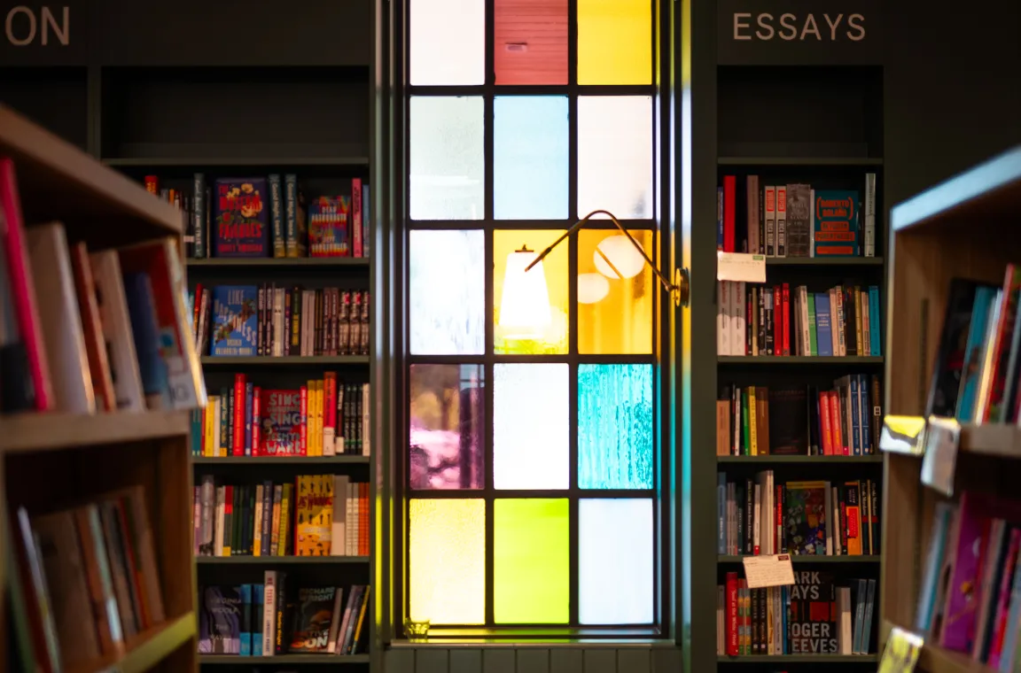 Colorful stained glass window framed by bookshelves at First Light Books, creating a warm and inviting reading atmosphere.