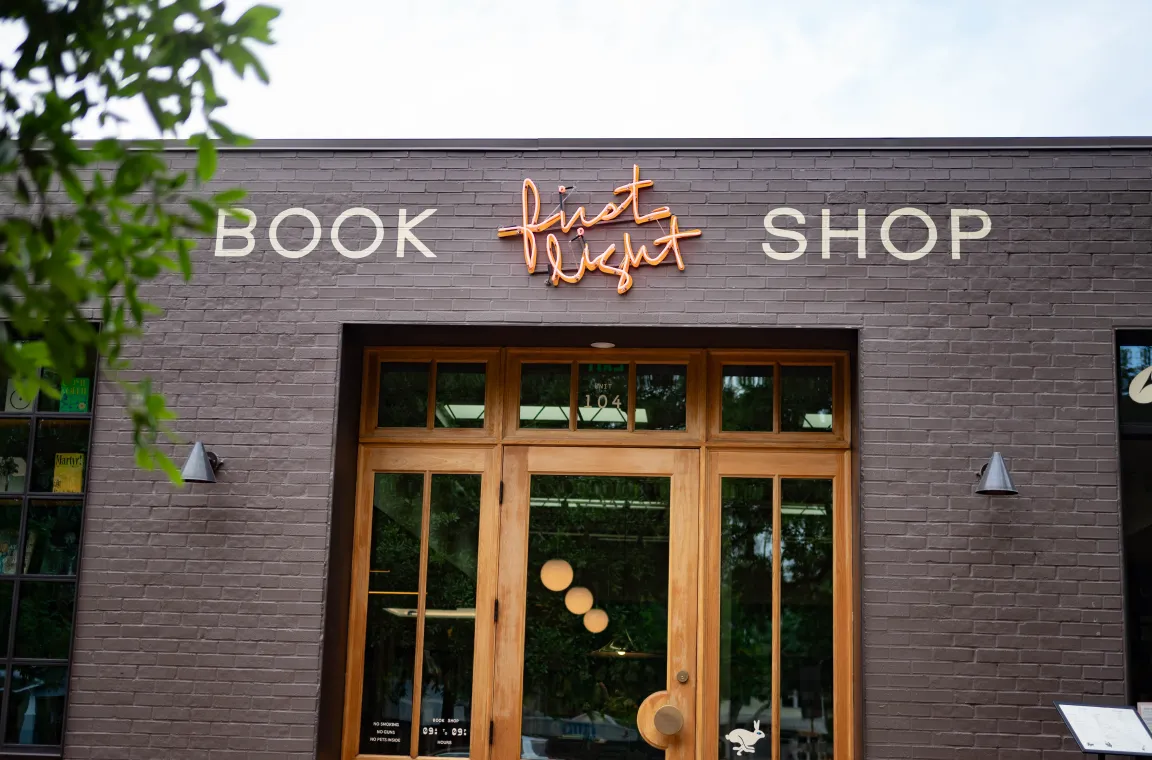 Exterior entrance of First Light Books featuring a modern brick storefront, wood-framed doors, and illuminated bookstore signage.