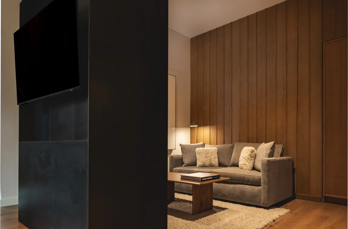 Cozy sitting area in a Larch House suite featuring warm wood paneling, a plush sofa, and a minimalist coffee table.