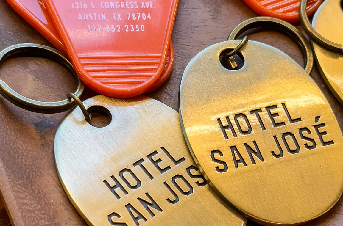 Vintage-style Hotel San José room key tags displayed on a wooden tray, featuring the hotel's signature branding and retro design.