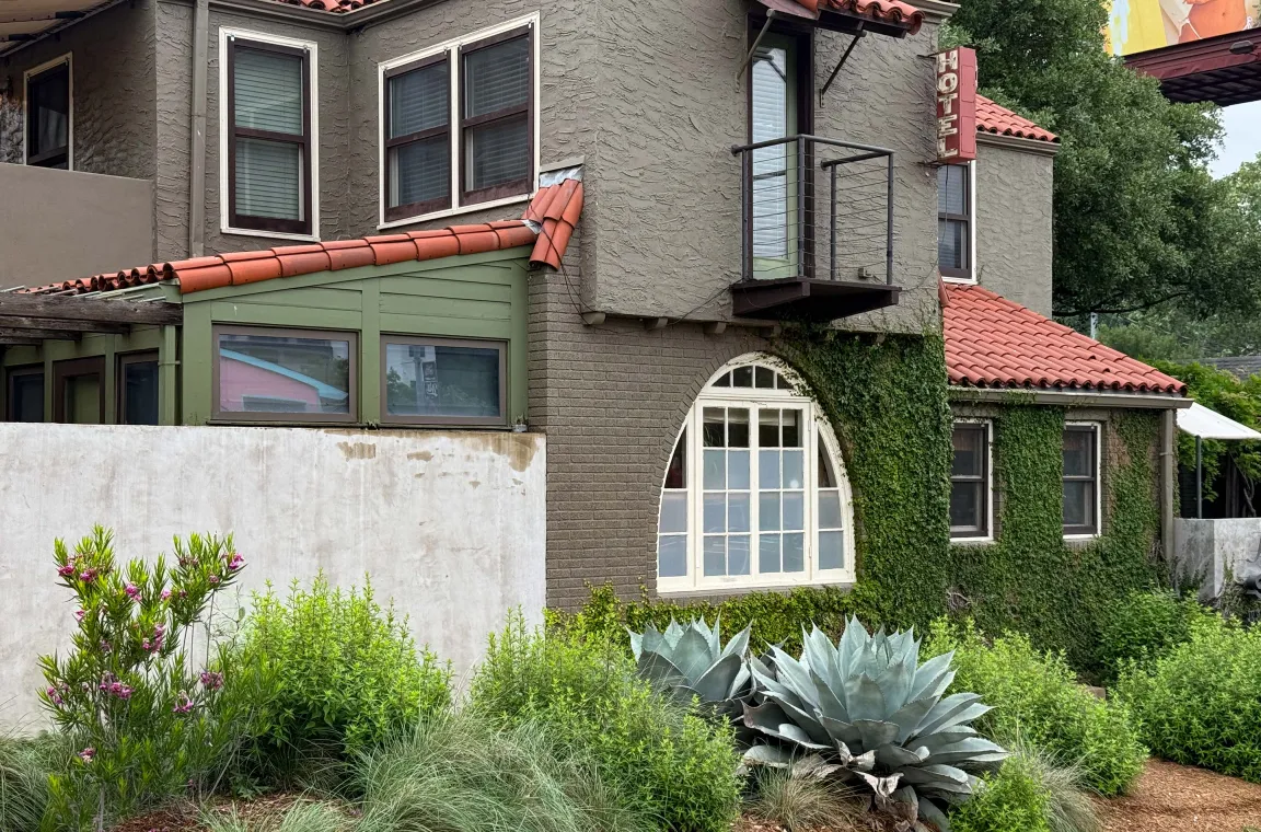 Exterior of Hotel San José featuring Spanish-style architecture, ivy-covered walls, red tile roofs, and lush landscaped gardens.