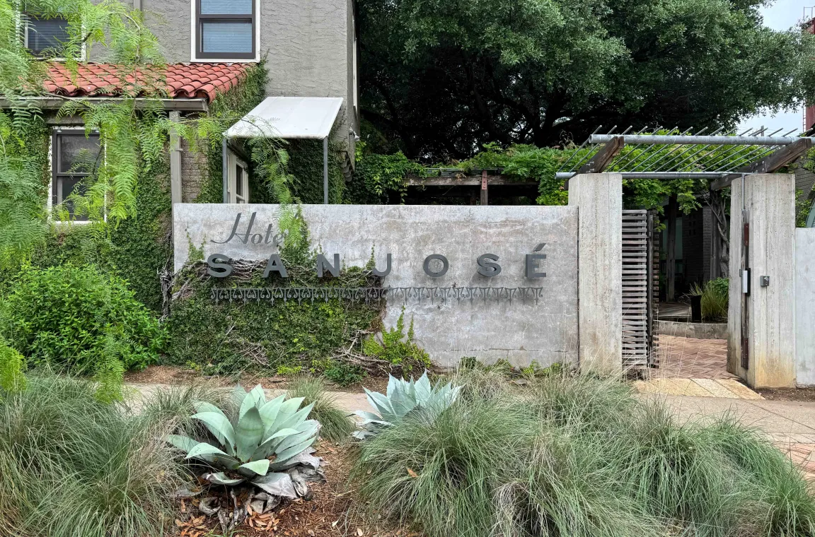 Hotel San José entrance featuring the iconic concrete sign, lush landscaping, and ivy-covered Spanish-style architecture.