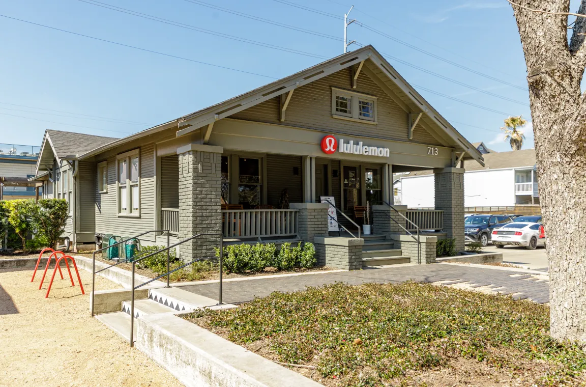 An earthy-green painted bungalow storefront for Lululemon, complete with a classic front porch, stone steps, and manicured landscaping.