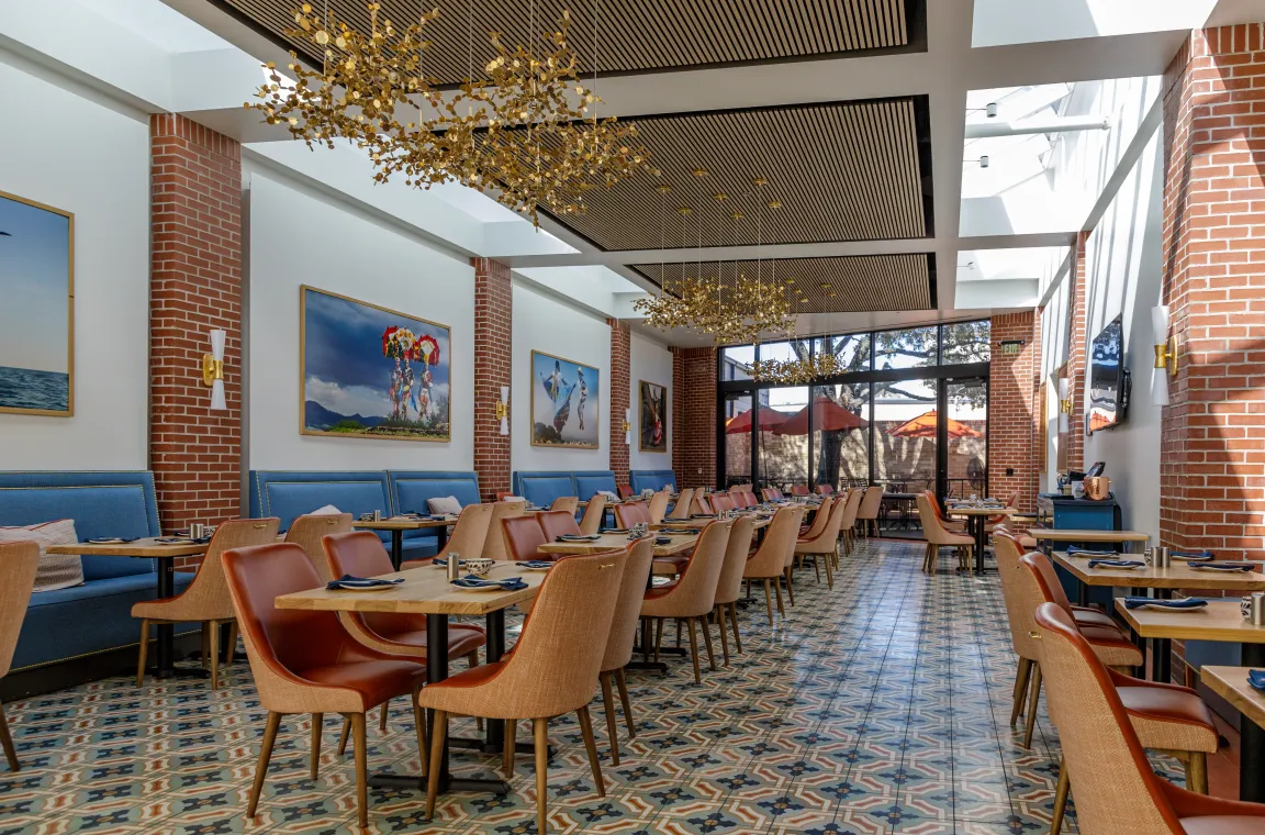 Interior dining room at Hugo's with high ceilings, decorative gold chandeliers, blue booth seating, and artwork featuring cultural figures displayed on exposed brick walls.