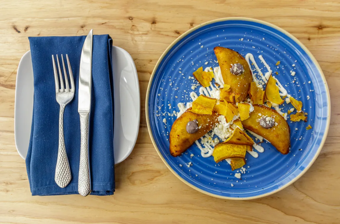 A plate of golden-brown empanadas garnished with white crumbles and plantain chips, served on a vibrant blue plate with a blue napkin and silverware.