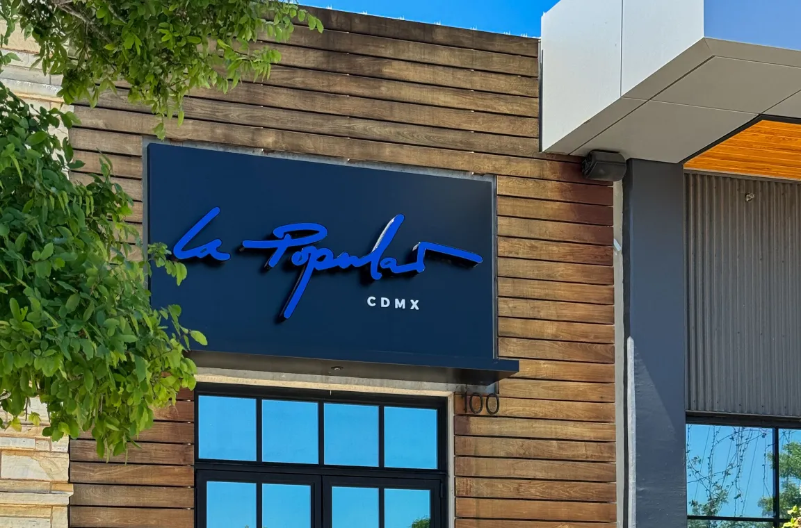 Close-up of the La Popular storefront sign featuring bold blue lettering on a modern wood-accented exterior.