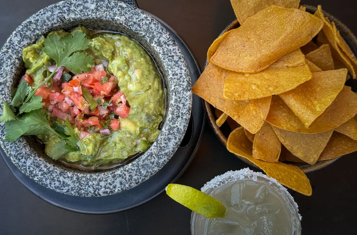 Fresh guacamole topped with pico de gallo and cilantro, served with crispy tortilla chips and a salt-rimmed margarita at La Popular.
