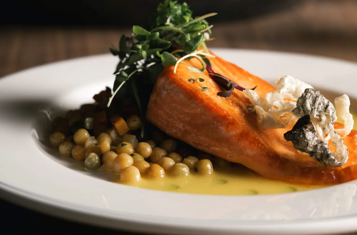 Pan-seared salmon served over pearl couscous in a buttery sauce, topped with microgreens and crisp vegetable garnish.