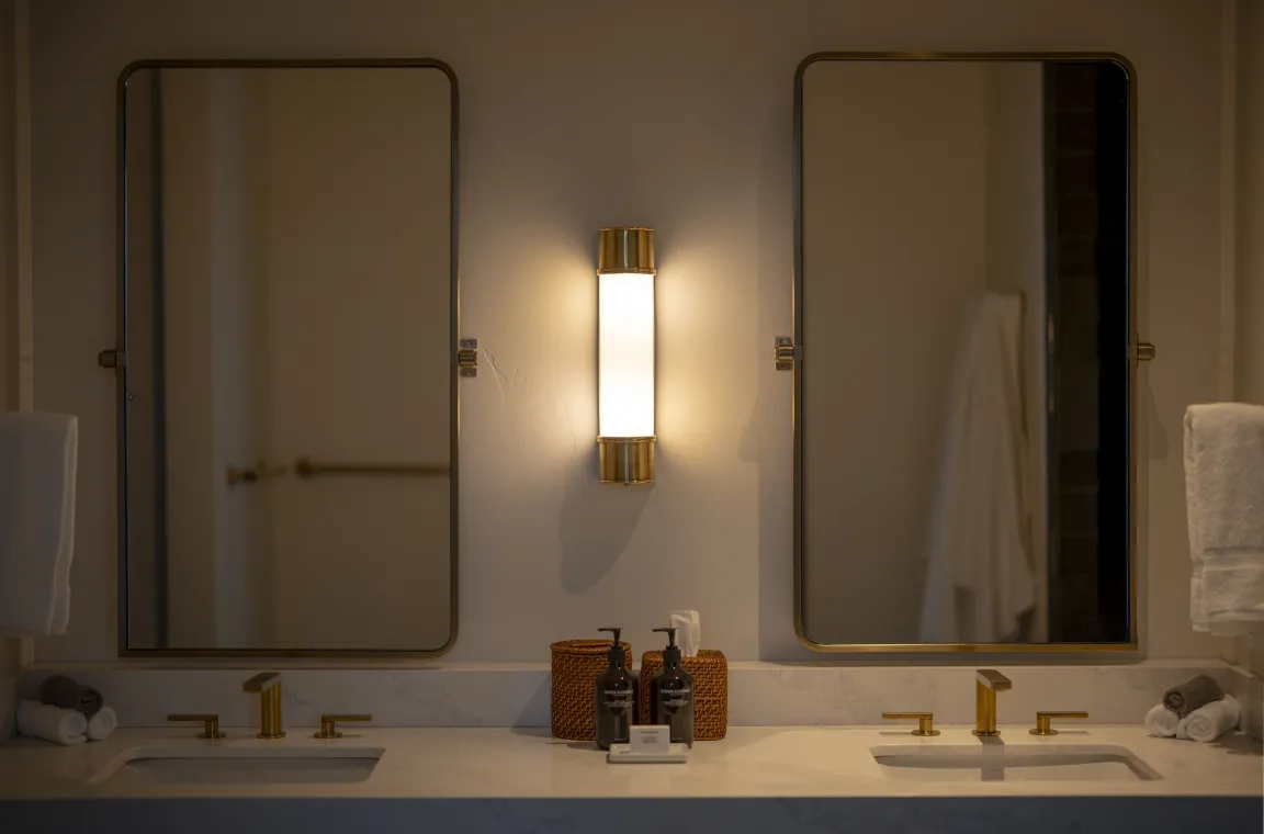 Double vanity bathroom at Larch House with brass fixtures, illuminated mirrors, and a marble countertop.