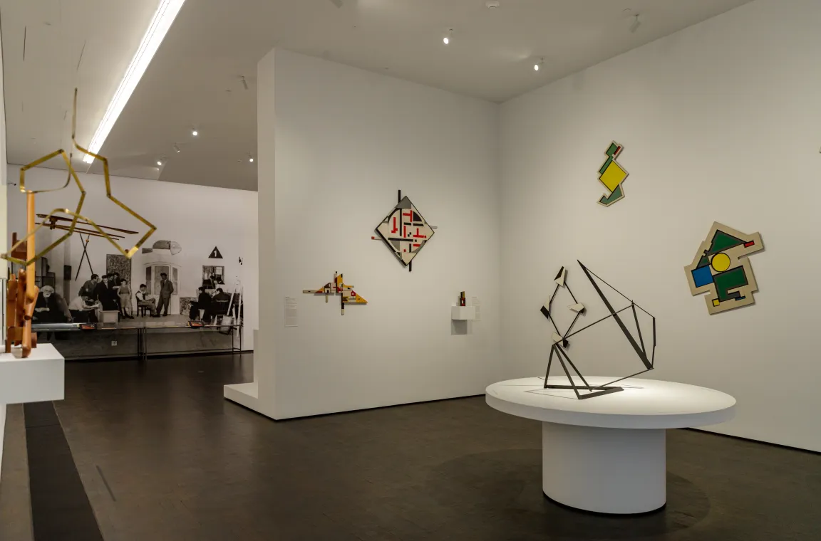 An exhibition room with dark wood flooring displaying various geometric, abstract wire and wall-mounted sculptures against white walls.