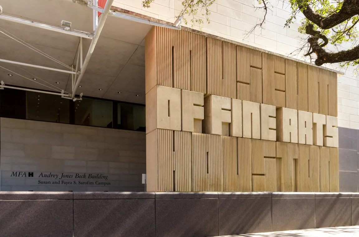 A prominent tan stone wall carved with large block lettering that spells out "MUSEUM OF FINE ARTS HOUSTON" at the entrance of the Audrey Jones Beck Building.