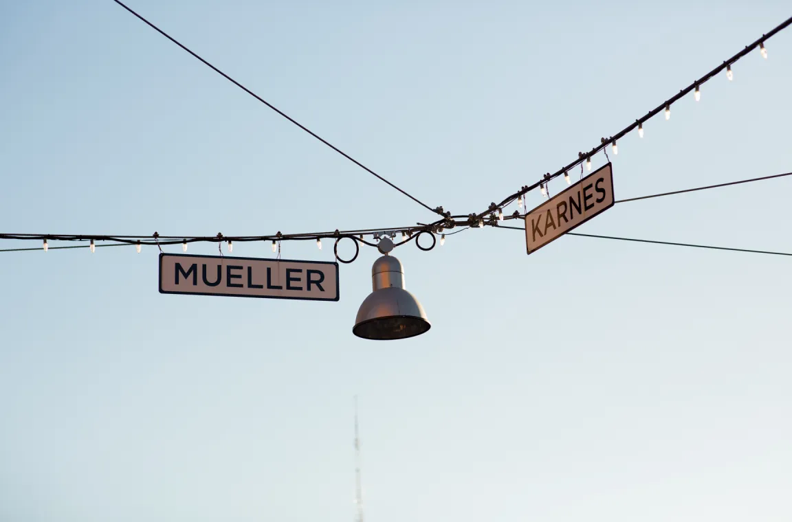 Decorative street signs for Mueller and Karnes streets hanging beneath string lights at the Pearl district in San Antonio.