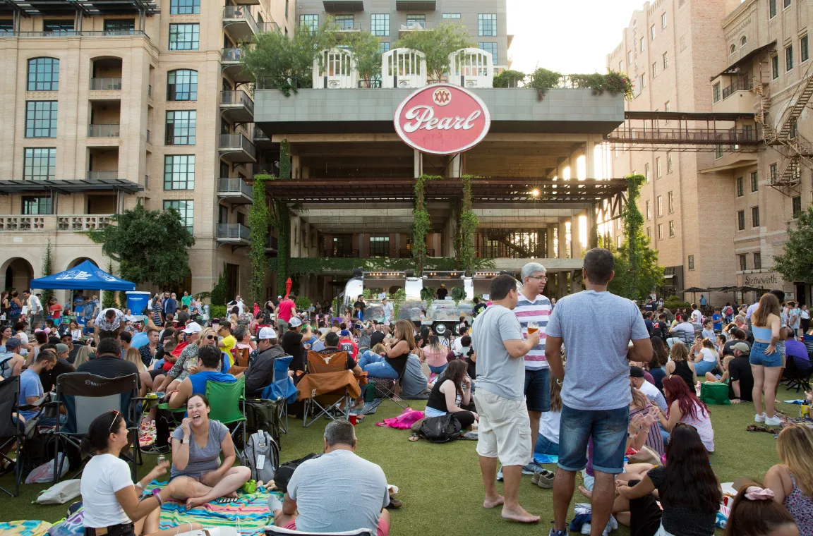Large crowd gathered on the lawn at Pearl in San Antonio for an outdoor community event, with the iconic Pearl sign and brewery buildings in the background.