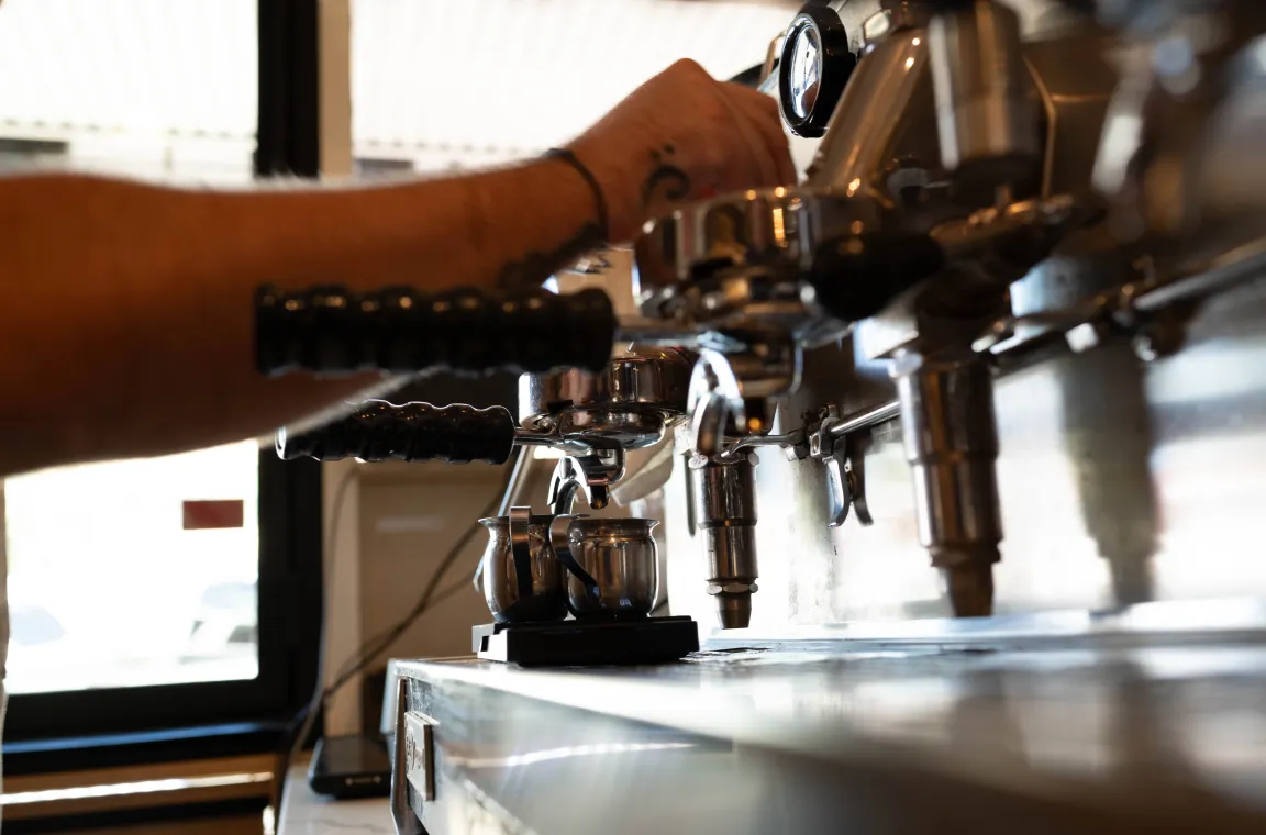Barista preparing espresso on a commercial espresso machine at the Tiny Grocer coffee bar.