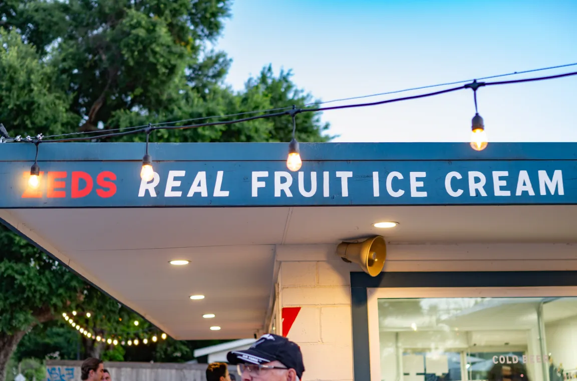 Close-up of the Zed's Real Fruit Ice Cream storefront signage illuminated with string lights at dusk.