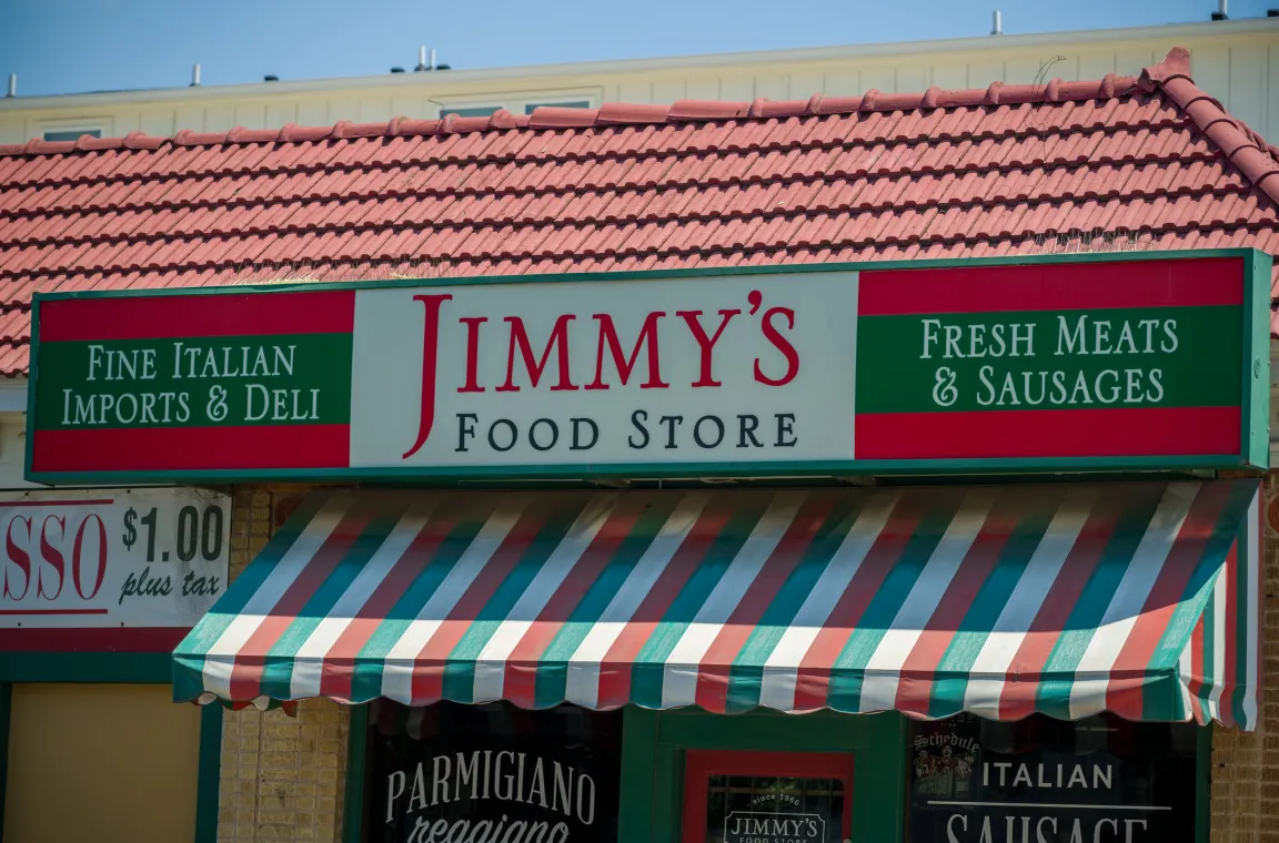 Exterior of Jimmy's Food Store in Dallas featuring its signature red, white, and green striped awning and signage advertising Italian imports, deli items, fresh meats, and sausages.
