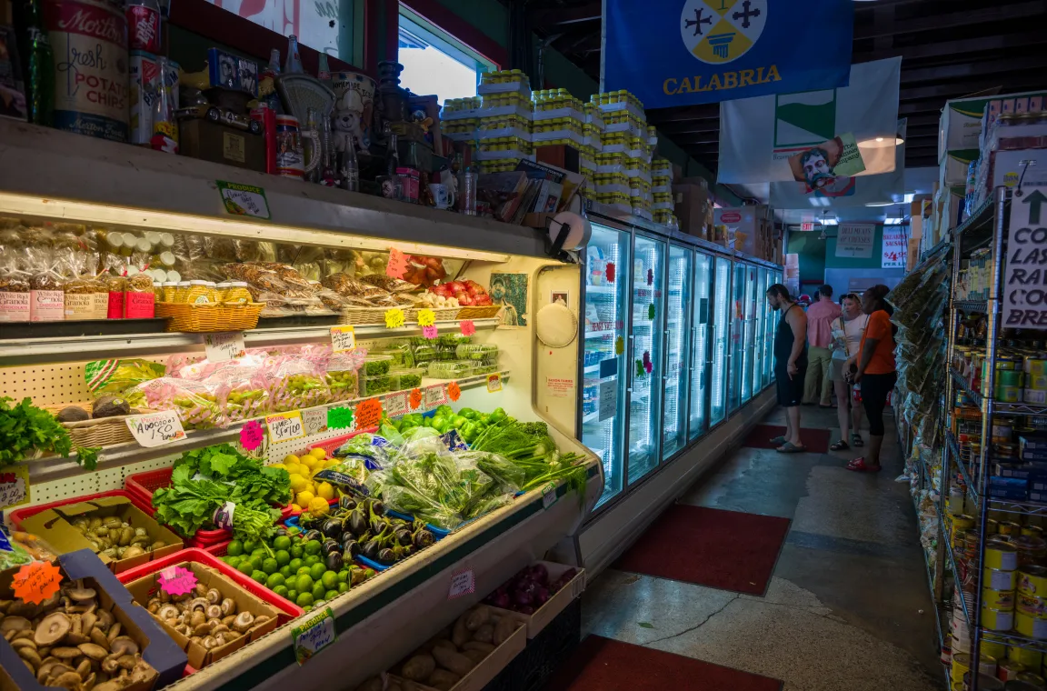 Interior produce section at Jimmy's Food Store with fresh vegetables, refrigerated Italian specialty foods, and shelves of imported grocery items lining the aisle.