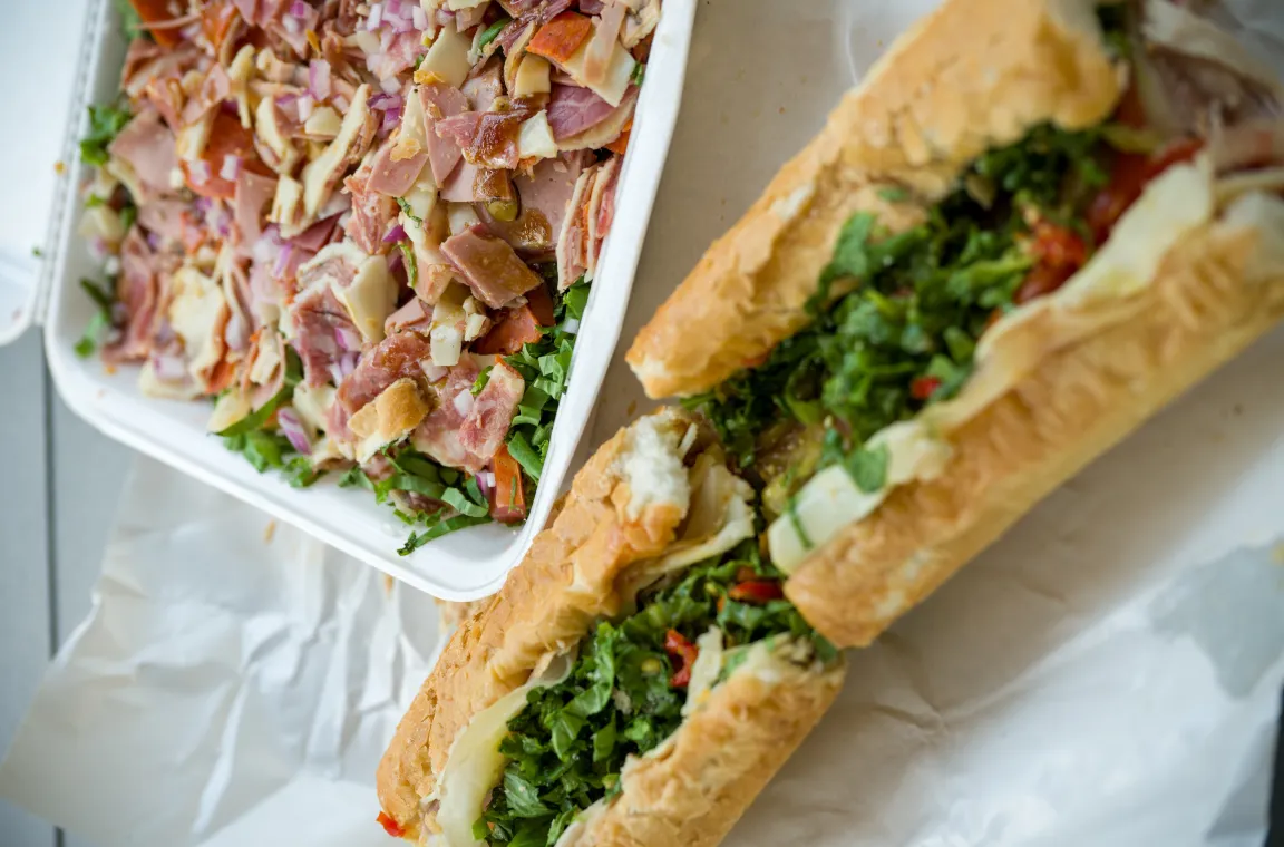 Italian sandwich filled with cured meats, cheese, and greens served alongside Jimmy's chopped Italian salad at Jimmy's Food Store in Dallas.