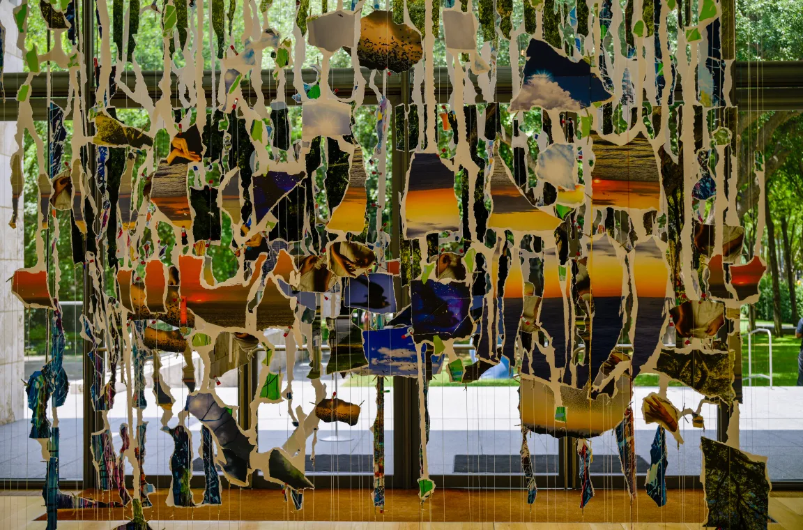 A suspended mixed-media installation composed of torn photographic fragments hanging in layers, creating a textured, immersive artwork in the museum's light-filled entrance gallery.