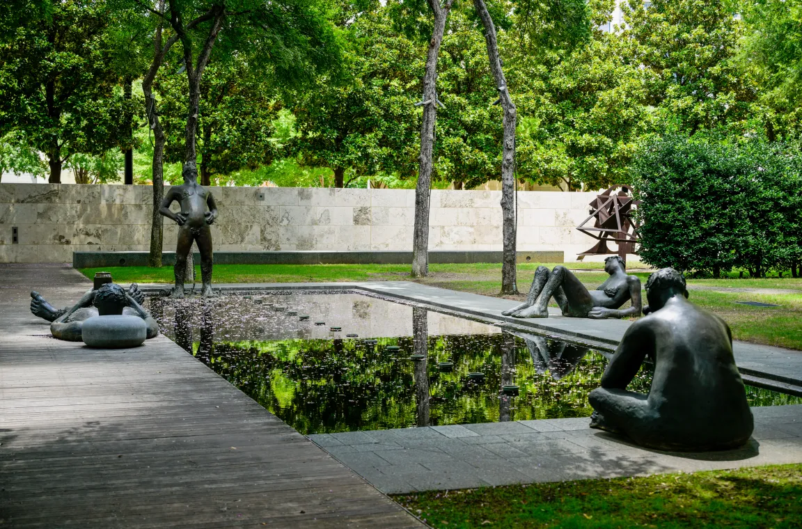 A serene reflecting pool surrounded by bronze figurative sculptures, demonstrating the Nasher's seamless blend of art, architecture, water, and landscape.