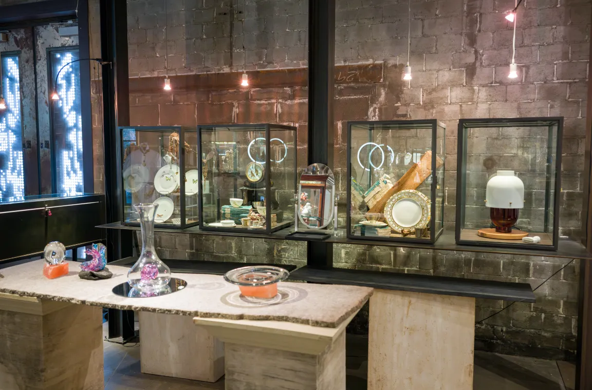 Display of curated home décor, ceramics, glassware, and tabletop accessories inside Grange Hall, arranged in glass cases against an industrial-style brick wall.