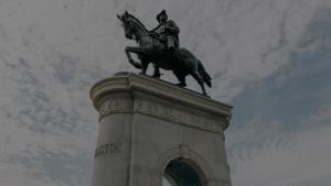 Low-angle view of the Sam Houston equestrian statue in Hermann Park, Houston, standing atop a stone pedestal against a partly cloudy Texas sky.