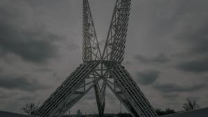 A low-angle shot looking down the pedestrian walkway of the Skydance Bridge under a moody, overcast sky, showcasing the soaring, white geometric steel wings of the monument overhead.