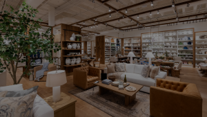 An interior shot of a Pottery Barn store, featuring chairs and sofa sets in the foreground, and shelves of various dishes and pottery in the background.